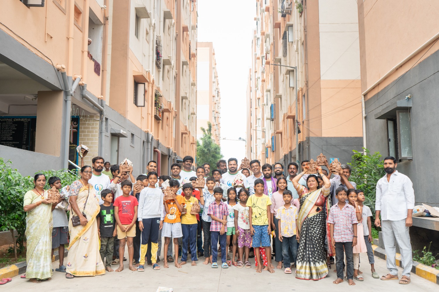 A large group of children and residents holding clay Ganesha idols on a street between housing blocks
