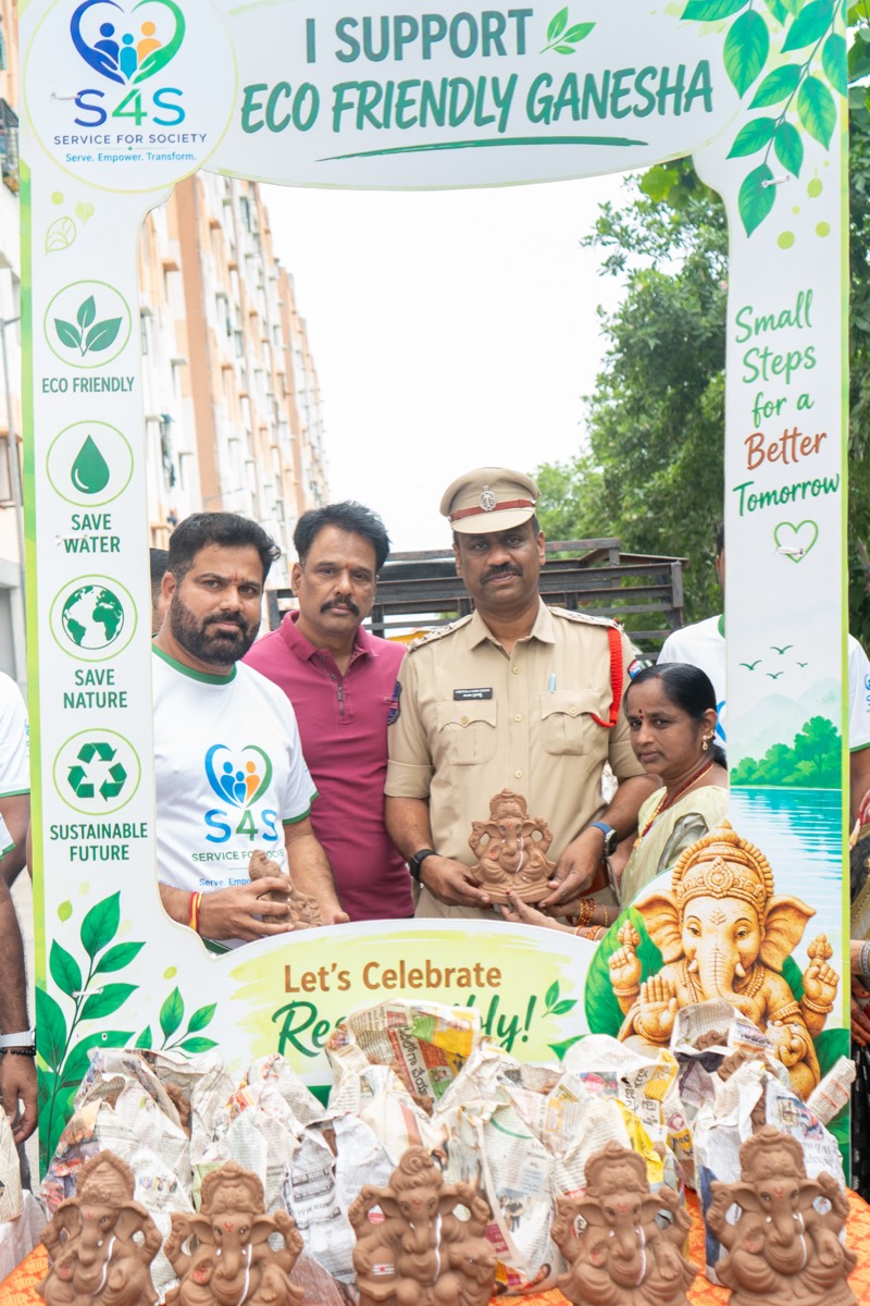A police officer in uniform holding a natural clay Ganesha idol alongside Service4Society volunteers and a resident at the distribution stall