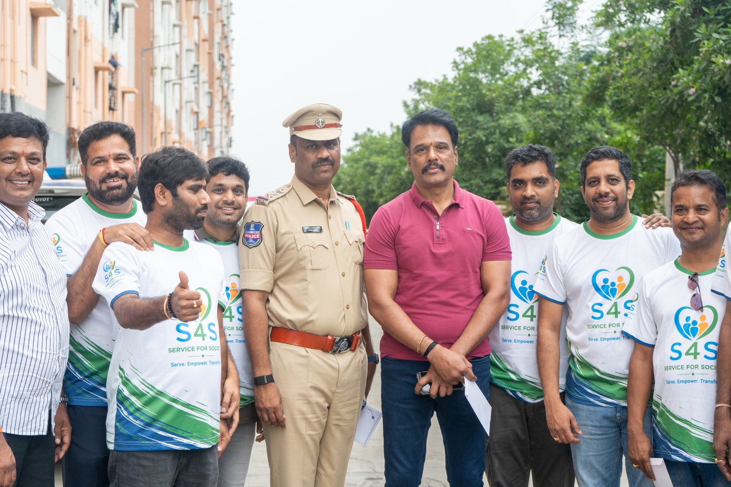 Service4Society volunteers in S4S t-shirts standing with a police officer on a street between apartment blocks